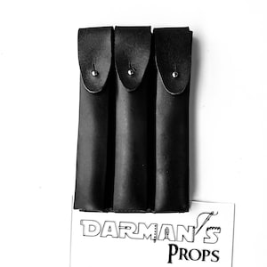 May include: Three black leather sheaths with silver poppers. The sheaths are lined up side by side. The sheaths are labelled "Darman's Props".