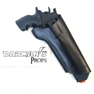 Könnte beinhalten: Schwarze Lederholster mit einer schwarzen Handfeuerwaffe. Die Handfeuerwaffe hat ein Adlerflügel-Design am Griff. Die Holster ist so konzipiert, dass sie die Handfeuerwaffe sicher hält. Das Bild enthält den Text "DARMAN'S PROPS".