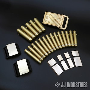 May include: A set of gold-coloured metal accessories, including a belt buckle, a row of small cylinders, and several rectangular pieces. The belt buckle has a geometric design and the cylinders have a silver trim. The rectangular pieces are flat and have a smooth surface.