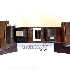 May include: A brown leather belt with multiple pouches and a silver buckle. The belt is designed to hold various accessories, including a flashlight, a lighter, and other small items. The belt is labeled "DARMAN'S PROPS".