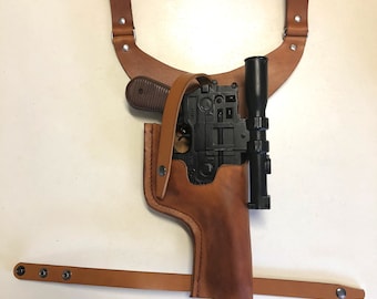 Op de afbeelding: Een bruine leren holster met een zwart pistool en een richtkijker. De holster heeft een band die over de schouder gaat en een riemband.