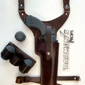 May include: A brown leather holster with a gray plastic gun and a brown leather strap. There are three gray plastic ammunition holders and a sticker that says "DARMAN'S Props".