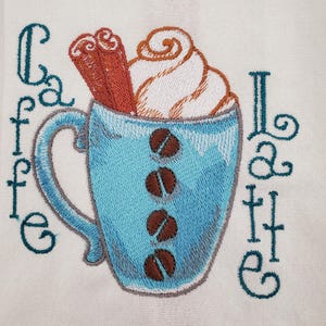May include: Embroidered design of a blue coffee cup filled with whipped cream, cinnamon sticks, and coffee beans. The words "Cafe Latte" are embroidered in teal on a white background. A cozy, coffee-themed design.