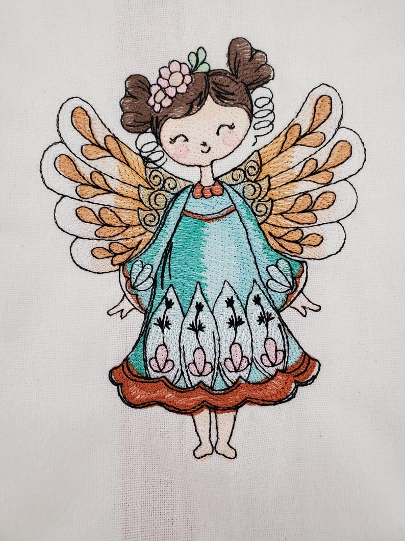May include: Embroidered image of a smiling fairy with brown hair, a flower crown, and large, detailed wings. The fairy wears a teal dress with floral accents and a brown trim. The artwork is on a white fabric background.