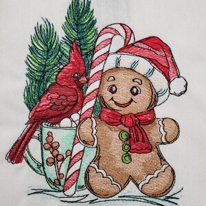 May include: Embroidered Christmas design featuring a red cardinal bird, a gingerbread man wearing a Santa hat and scarf, a candy cane, and a mug of hot cocoa with marshmallows. The design is set against a backdrop of evergreen branches.