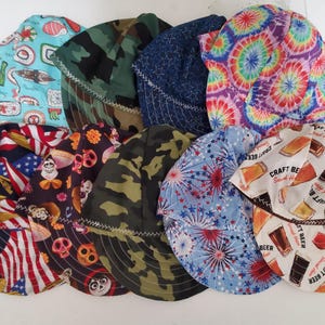 May include: A collection of colorful welding caps with various patterns, including sushi, camouflage, tie-dye, American flags, skulls, and beer glasses. These caps are designed to protect the wearer during welding.