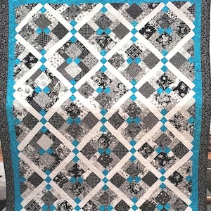 May include: A quilt with a diamond pattern in black, white, and turquoise. The quilt is made of many different fabrics with various patterns.