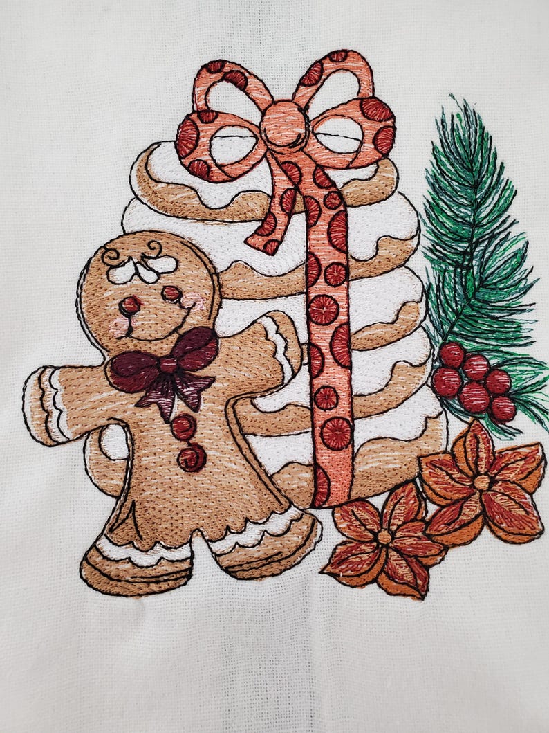 May include: Embroidered Christmas design featuring a gingerbread man with a bow tie, a stack of cookies, a bow, and a sprig of evergreen. The design also includes two orange flowers and red berries. The embroidery is on a white background.