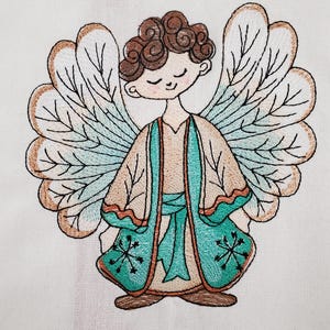 May include: Embroidered image of a serene angel with brown curly hair, closed eyes, and large detailed wings. The angel wears a tan robe with teal accents and a teal sash. The wings have a tan and teal color scheme.