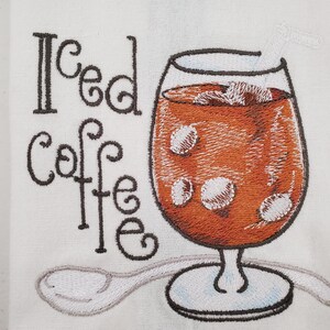May include: Embroidered white fabric features a glass of iced coffee with ice cubes and a straw. The words "Iced Coffee" are embroidered in black script. A spoon is embroidered below the glass.