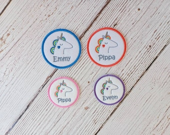May include: Four round iron-on patches with a white unicorn design and rainbow mane. Each patch has a different colored border and a name: Emmy, Pippa, Pippa, and Evelyn.