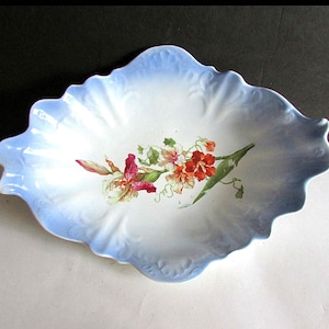 May include: A white porcelain oval serving dish with a blue rim and a floral design of pink, yellow, and green flowers.