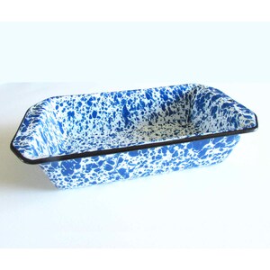 May include: A rectangular baking pan featuring a white base with a blue speckled enamel finish. The edges of the pan are reinforced with a thin, dark black rim that outlines the entire perimeter of the vessel, providing a clear contrast.