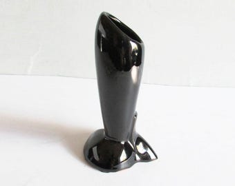 Puede incluir: Un jarrón negro brillante de cerámica con una base acampanada y una abertura curva y asimétrica. El jarrón tiene una superficie lisa y reflectante y un diseño escultural único. El jarrón mide aproximadamente 15 cm de alto.