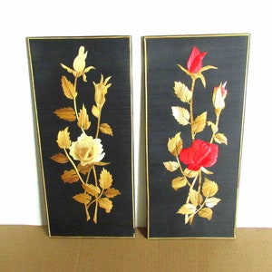 May include: Two framed wall art pieces with black backgrounds and gold leaf roses. One rose is white and the other is red.