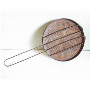 May include: A rusty metal grill pan with a long handle. The pan has a round, perforated surface with four raised bars for grilling.