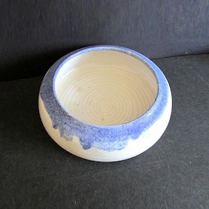 May include: A white ceramic bowl with a blue rim. The bowl has a slightly rounded shape and a smooth, glazed finish.