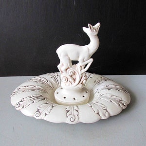 May include: White ceramic deer figurine on a white ceramic dish with a decorative leaf pattern. The dish has a center hole with small holes around it.