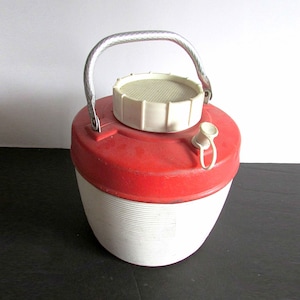 May include: A red and white vintage insulated beverage jug with a silver handle and a white lid. The jug has a ribbed design.