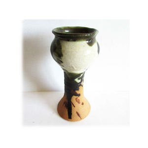 May include: A handmade ceramic vase with a bulbous body and a tall, slender stem. The vase features a speckled beige and white body with dark green and black accents. The rim is dark green, and the base is a speckled tan color.