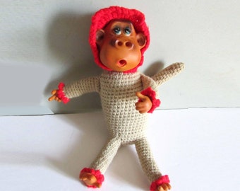 May include: A crocheted monkey toy with a red hat and red accents on the arms and legs. The monkey has a brown face and large eyes.