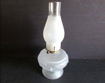 May include: A frosted glass oil lamp with a floral design on the base. The lamp has a clear glass chimney and a brass wick holder.
