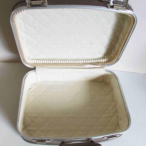 Puede incluir: Una maleta vintage plateada y marr&oacute;n con un forro acolchado blanco. La maleta est&aacute; abierta y el interior es visible.