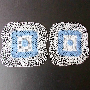 May include: Two white crocheted doilies with blue and white square designs in the center.