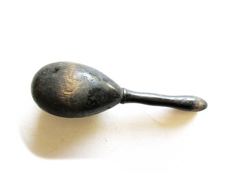 May include: A wooden egg-shaped maraca with a black handle. The maraca is made of dark wood and has a smooth, polished finish.