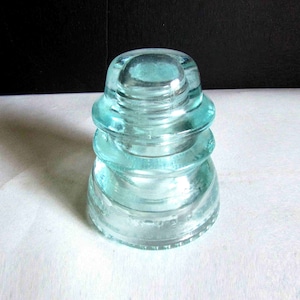 May include: A vintage glass insulator with four tiers, each with a slightly different shape. The insulator is a light blue color and has a smooth, glossy finish.