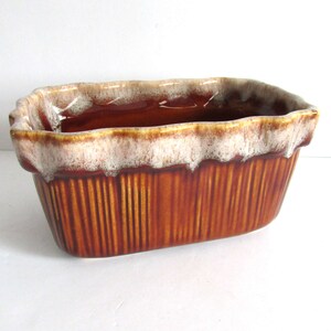May include: A brown and white glazed ceramic planter with a ruffled rim and vertical lines.