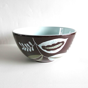 May include: A decorative ceramic bowl with a brown exterior and a light blue interior. The bowl features a leaf design in white and green. The bowl is suitable for serving food or as a decorative piece.