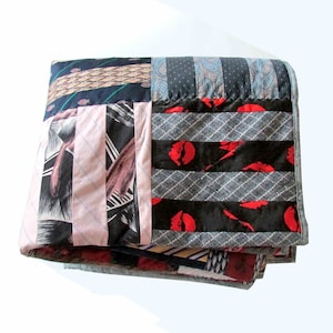 May include: A patchwork quilt made from repurposed neckties. The quilt is made up of various colors and patterns, including red, blue, black, and white. The quilt is folded and lying on a white surface.
