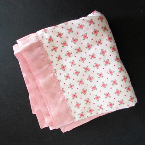 May include: A pink and white baby blanket with a floral pattern. The blanket has a pink satin border.