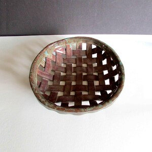 May include: A handcrafted ceramic basket with a woven design. The basket features a deep burgundy color with a textured surface and a turquoise rim. The open weave allows for air circulation, making it suitable for displaying fruit or other items.