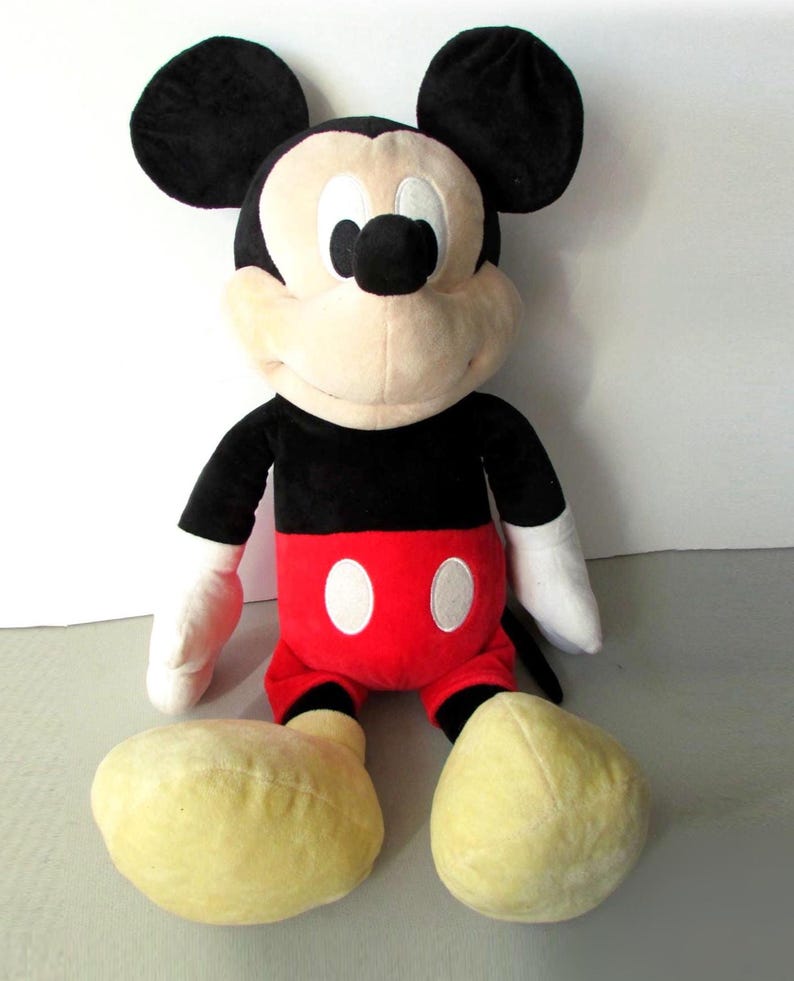 May include: A plush Mickey Mouse toy. The iconic character is depicted with black ears, a black torso, red shorts with white buttons, white gloves, and large yellow feet. The toy is soft and cuddly, perfect for children and Disney fans.