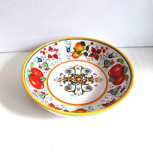 May include: A white ceramic serving bowl with a yellow rim and colorful floral and fruit designs. The bowl features red tomatoes, yellow pears, and red flowers. The interior has a central decorative pattern in blue, yellow, and orange.