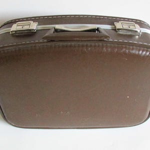 Puede incluir: Una maleta vintage marr&oacute;n con cierres plateados y un asa. La maleta tiene una costura cosida alrededor del borde.