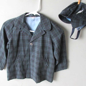 May include: A plaid jacket and matching cap in shades of green and black. The jacket has a single button closure and two pockets. The cap has a small feather detail.