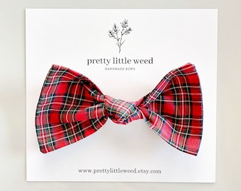 May include: A red plaid fabric bow with green, yellow, and black lines, centered on a white display card. The card features the text pretty little weed HANDMADE BOWS and the website address www.prettylittleweed.etsy.com with a small botanical icon.