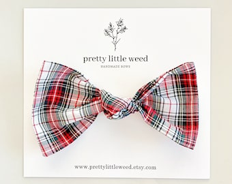 May include: A fabric bow with a red, white, green, and black plaid pattern attached to a white display card. The card features the text pretty little weed HANDMADE BOWS and the website address www.prettylittleweed.etsy.com with a small botanical icon.
