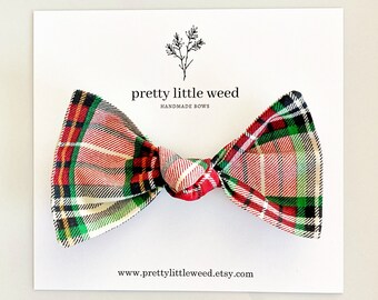 May include: A fabric bow with a red, green, white, and black plaid pattern attached to a white display card. The card features a black line drawing of a plant and the text "pretty little weed HANDMADE BOWS" and "www.prettylittleweed.etsy.com".