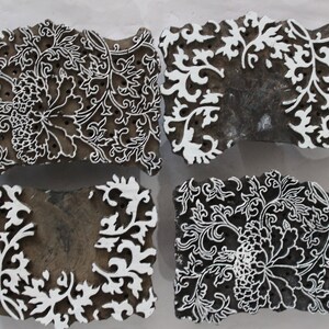 May include: Four wooden printing blocks with intricate white floral designs. The blocks are carved with a variety of patterns, including leaves, flowers, and vines.