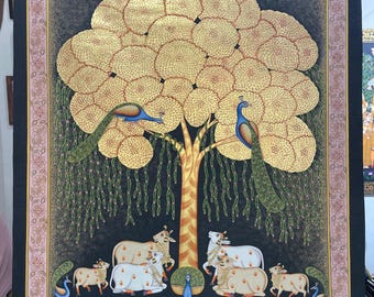 Puede incluir: Una pintura ornamentada con un árbol dorado con hojas circulares en capas. Dos pavos reales se posan en el árbol, con vacas y un pavo real en la base. La pintura tiene un borde floral rosa y un fondo oscuro.