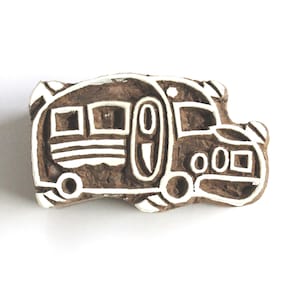 Könnte beinhalten: Ein brauner Holzstempel in Form eines Wohnwagens. Der Stempel hat weiße Umrisse und Details, einschließlich Fenster, Räder und eine Tür. Das Wohnwagendesign ist in einem charmanten, rustikalen Stil gehalten.