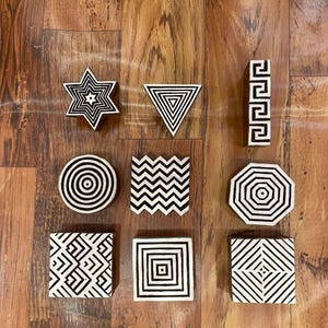 May include: Set of ten wooden printing blocks with geometric designs in black and white. The designs include a star, triangle, zig zag, circle, octagon, and various squares.