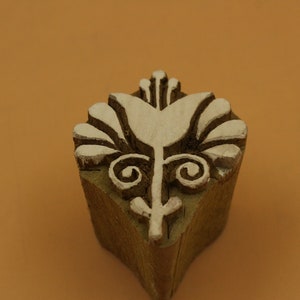 May include: A wooden block printing stamp with a white floral design. The design features a stylized flower with a central stem and leaves.
