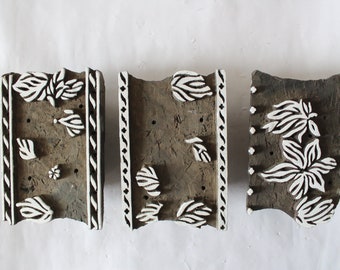 May include: Three wooden printing blocks with intricate floral designs carved into them. The designs are painted white and the blocks are a dark brown color.