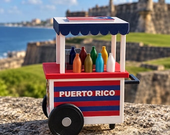 Puede incluir: Un carrito de madera en miniatura con un diseño de rayas rojas, blancas y azules con el texto PUERTO RICO en el lateral. El carrito tiene un toldo azul festoneado, ruedas negras y una exhibición de ocho botellas pequeñas y coloridas.