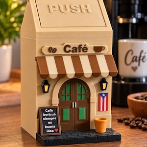 May include: A beige, house-shaped trash bin with a swinging lid labeled PUSH. The front features a brown and white striped awning, a sign reading Café with coffee icons, a brown door, two small lanterns, a Puerto Rican flag, and a sign reading Café boricua siempre es buena idea.